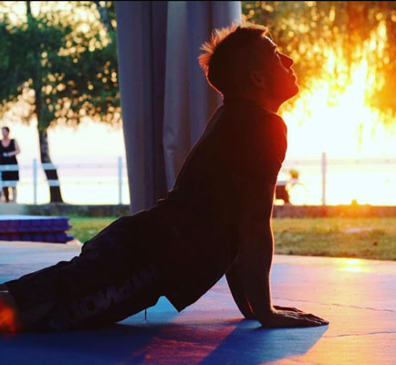 A practitioner stretching into an upward-facing pose on the outdoor mat, backlit by the sunset over Lake Balaton