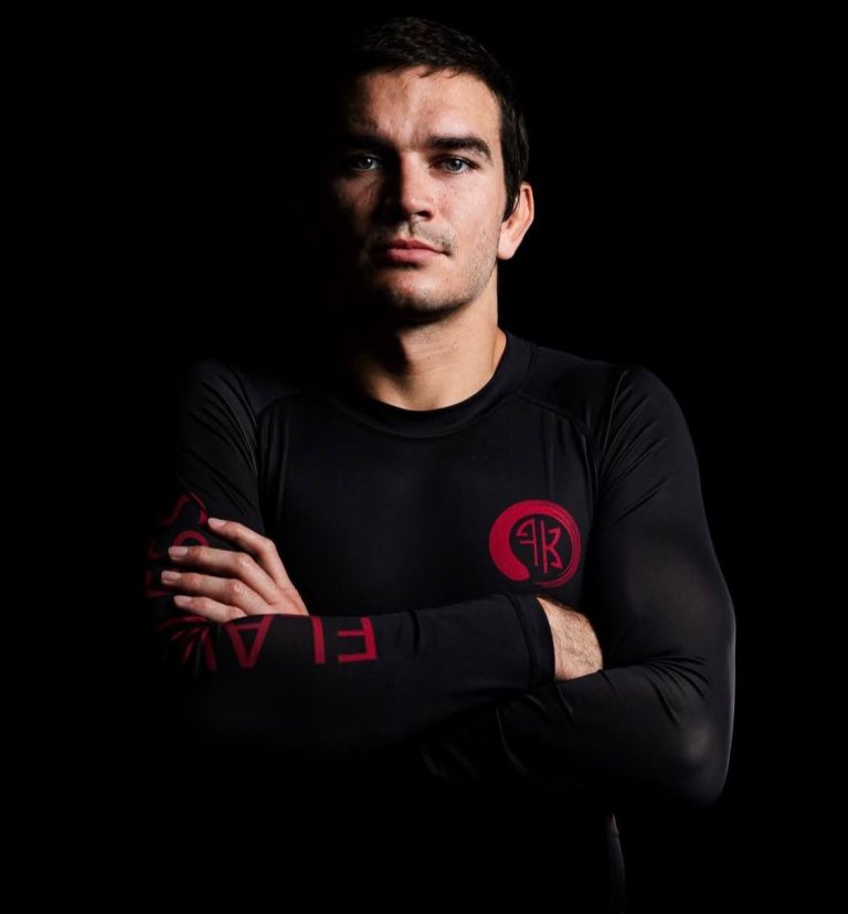 Kieran Kichuk, black belt professor, arms folded in a black no-gi rash guard